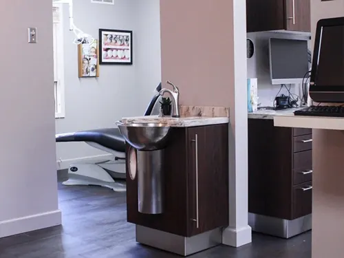 A treatment room at McNeil Dental, with a stainless sink and a dental chair beyond.